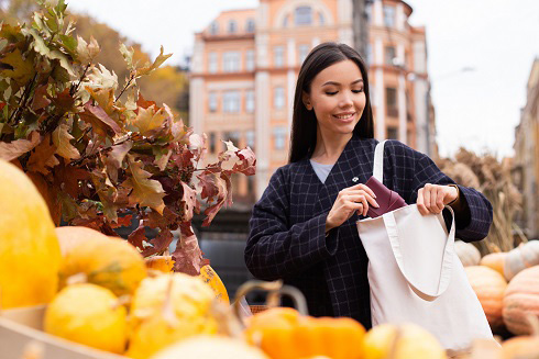 a woman smiling with her tote bag in front of oranges